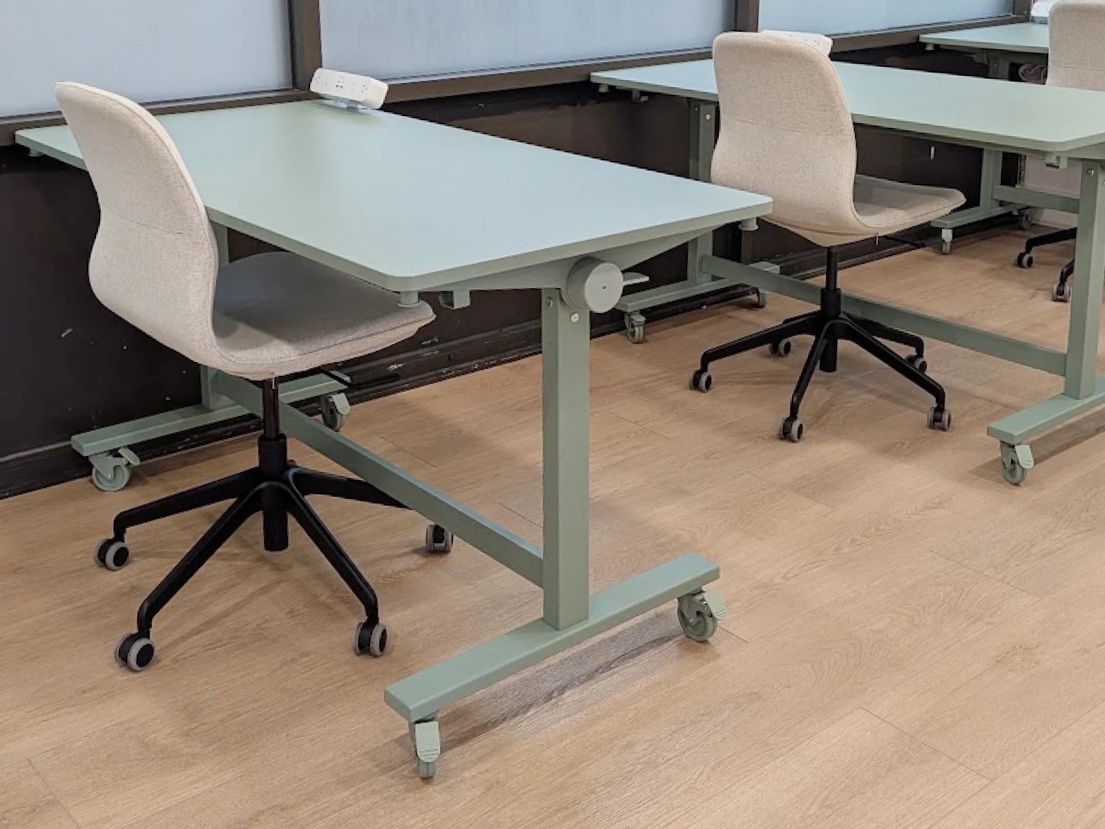 Dedicated desks at HudsonDesk — sage-green height-adjustable desks with cream upholstered task chairs